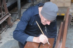 ... and having secured a new plank to another bench, carefully paints the bolt heads to make them less obvious.
