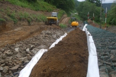 … which is tied to the back of the gabions. Suitable material is excavated and placed on the geotextile to keep it down in the breeze, which is then lapped back over again, and the next layer of foundation stone laid beyond.